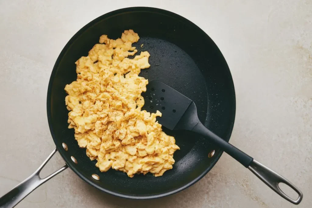 Folding scrambled eggs with a spatula in a skillet, moving eggs from the edges to the center to keep them soft and prevent overcooking