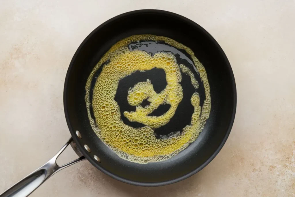 Heating a non-stick skillet over medium heat with a pat of butter melting in preparation for cooking scrambled eggs with cottage cheese