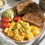 Creamy scrambled eggs with cottage cheese served with toasted bread and a fresh salad garnish, presented on a white plate for a wholesome breakfast.